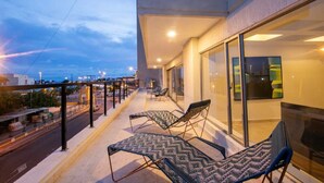 A balcony with two lounge chairs, a glass door, and a view of the cityscape. - Clock Tower PH · PH in the historic center (Cartagena)