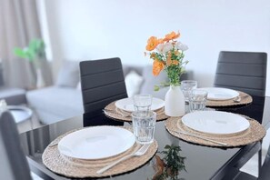Una mesa de comedor dispuesta con platos, cubiertos y vasos, con un jarrón de flores en el centro.