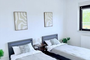 Habitación de hotel con dos camas, una mesita de noche con lámpara y dos cuadros abstractos colgados en la pared.