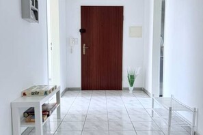 A hallway with a wooden door, a white console table with books, a potted plant, and a metal drying rack.