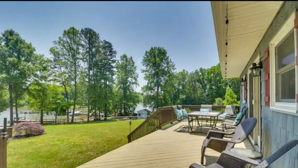 A wooden deck with outdoor furniture, a covered area, and a view of trees and a lake. - Lakefront 3-bedroom chalet with private dock (Louisa)