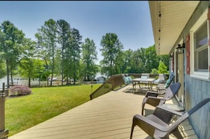 Une terrasse en bois avec des meubles d’extérieur, un espace abrité et une vue sur les arbres et un lac.