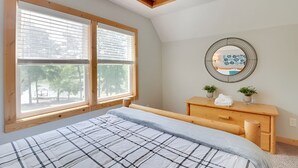 A bedroom with a bed, a wooden dresser, a round mirror, and two windows with blinds. - Lakefront 3-bedroom chalet with private dock (Louisa)