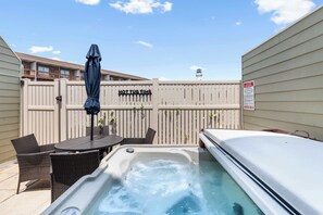 Un espace avec un bain à remous, entouré d’une clôture en bois, comprenant une table avec des chaises et un parasol.
