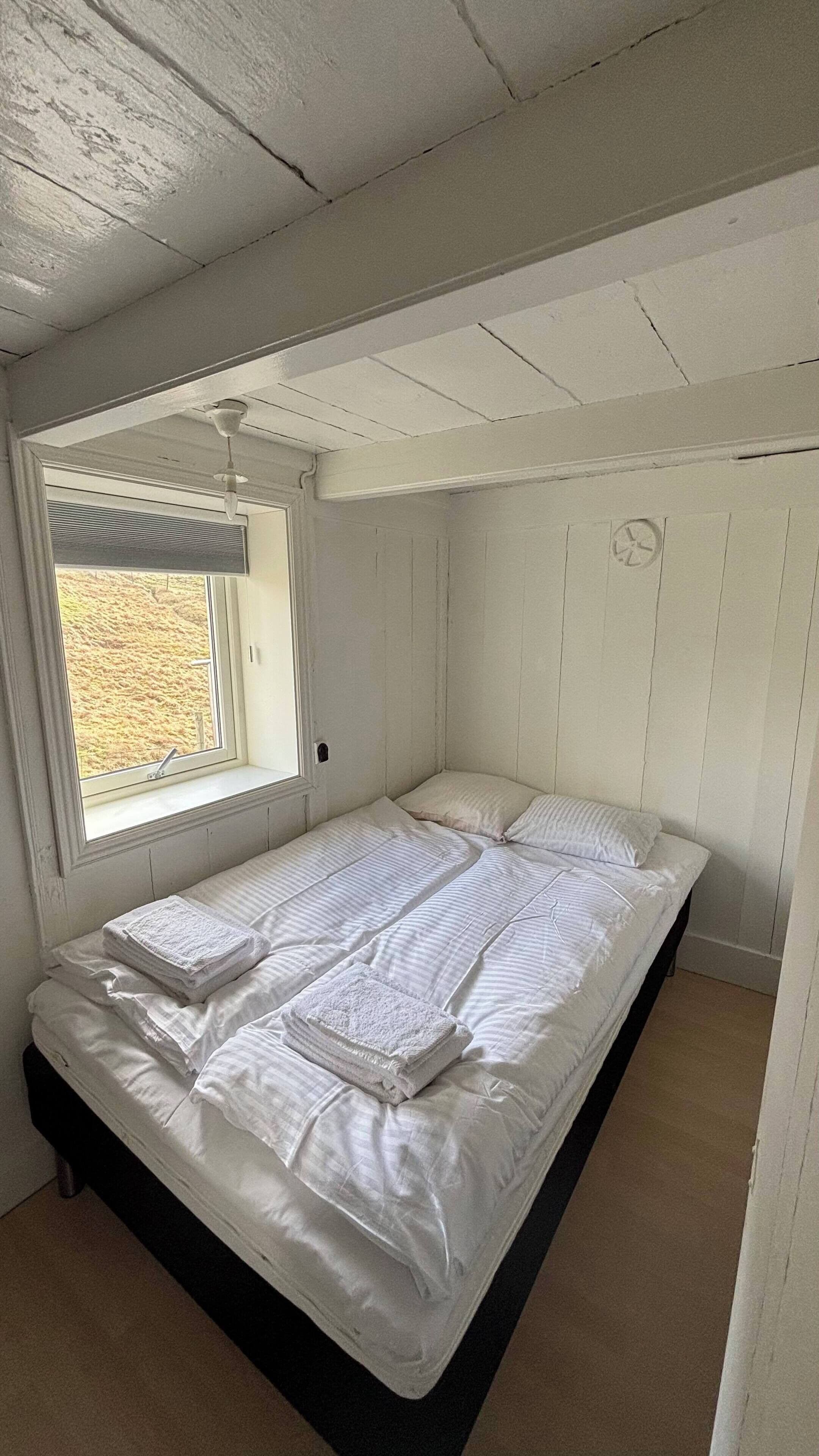 A single bed with white linens, a window with blinds, and a ceiling fan.