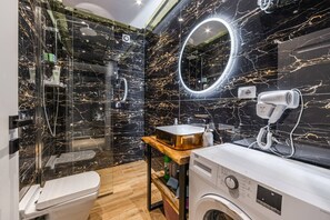Une salle de bain moderne dotée d’une douche à parois de verre, d’un meuble-lavabo avec miroir, d’un sèche-cheveux et d’un lave-linge.
