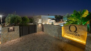 A stone-walled entrance to Omega Luxury Villa with a sign, a gated driveway, and a pool area visible in the background. - Villa Omega - Two Bedroom Villa, Sleeps 4 (Ditiki Mani)