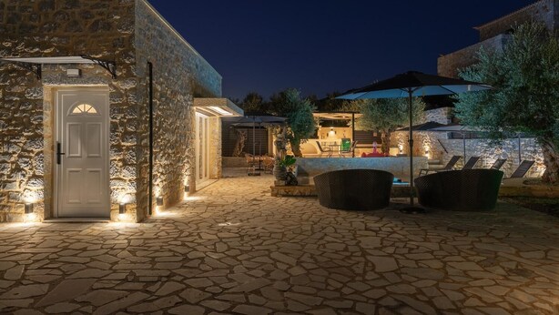 A stone building with a door, outdoor seating, and a pool area at night. - Villa Omega - Two Bedroom Villa, Sleeps 4 (Ditiki Mani)