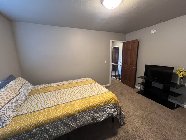 A bedroom with a bed, a television on a stand, and a door leading to a balcony.