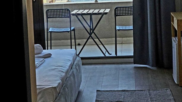 Una habitación con cama, una mesita, dos sillas, vista al mar y un balcón con barandilla.