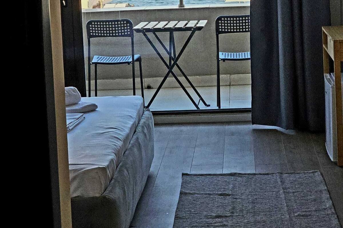 A room with a bed, a small table, two chairs, a view of the sea, and a balcony with a railing.
