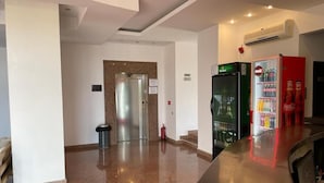 Vestíbulo de hotel con mostrador de recepción, refrigerador, máquina expendedora y extintor.
