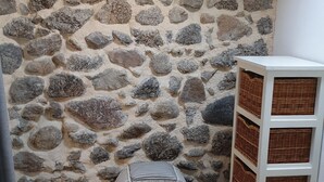 A room with a stone wall, a wicker ottoman, a white storage unit with baskets, and a bed with a patterned quilt. - La Félicité: the river, nature, time to yourself. (duniere sur eyrieux)