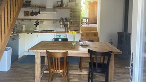 A kitchen with a wooden table, two chairs, a stove, and a hanging light fixture. - La Félicité: the river, nature, time to yourself. (duniere sur eyrieux)