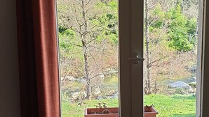 A room with a window overlooking a garden, a door, and a chair with a cushion. - La Félicité: the river, nature, time to yourself. (duniere sur eyrieux)