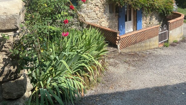 A stone building with blue shutters, a gravel driveway, and a garden with green plants and red flowers. - La Félicité: the river, nature, time to yourself. (duniere sur eyrieux)