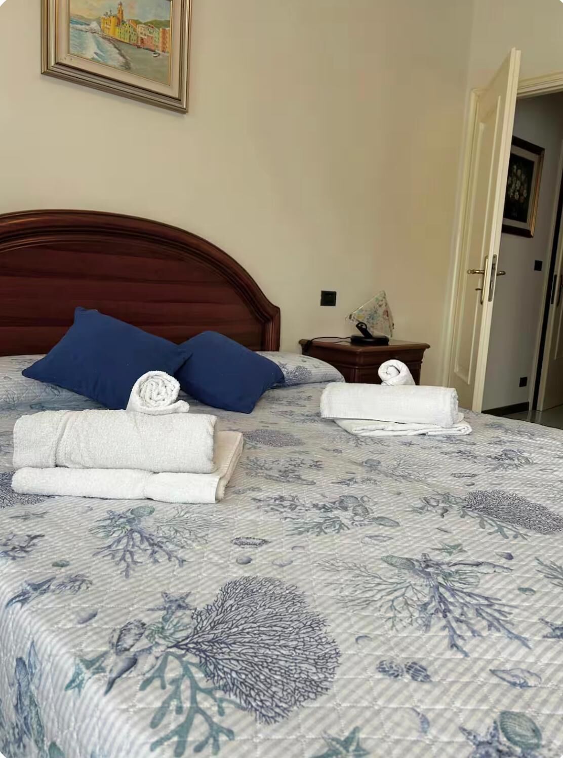 Un lit bien fait, recouvert d’une couvre-lit à motifs floraux, avec deux oreillers bleus et des serviettes blanches pliées.