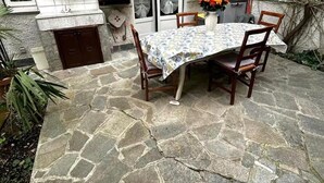 A stone patio with a table and chairs, a small sink, and a window with curtains.