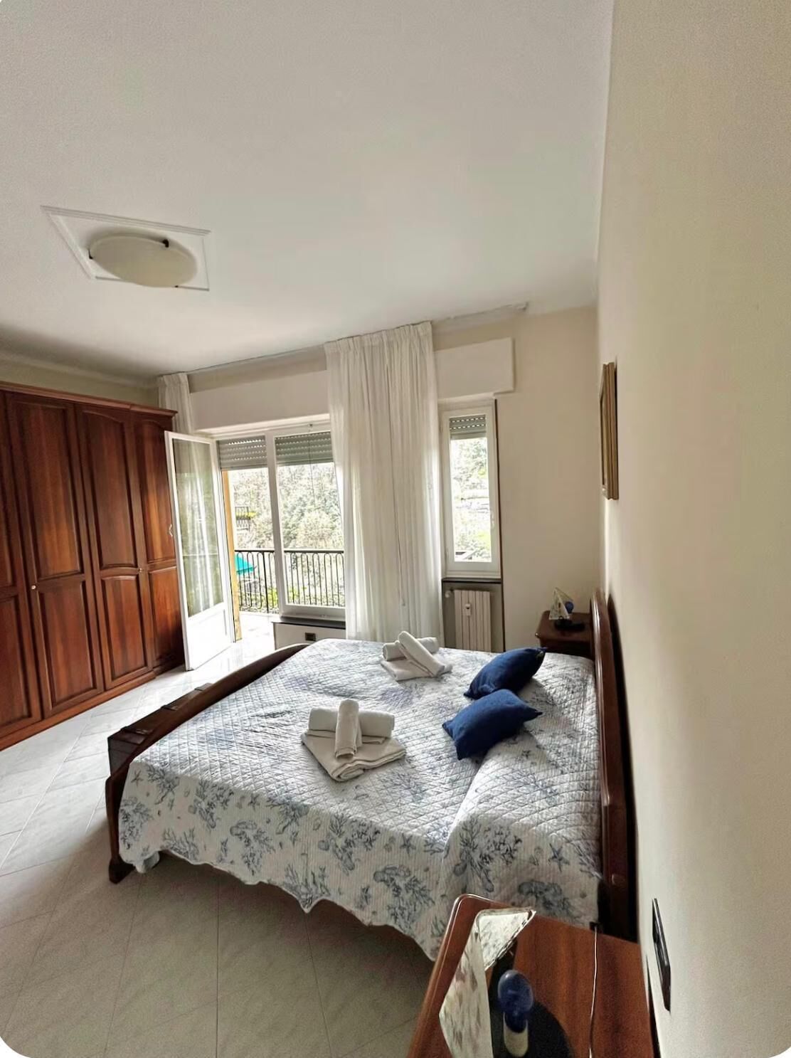 Une chambre à coucher comprenant un lit, une table de chevet, une armoire en bois et une fenêtre avec des rideaux.