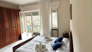 A bedroom with a bed, a nightstand, a wooden wardrobe, and a window with curtains.