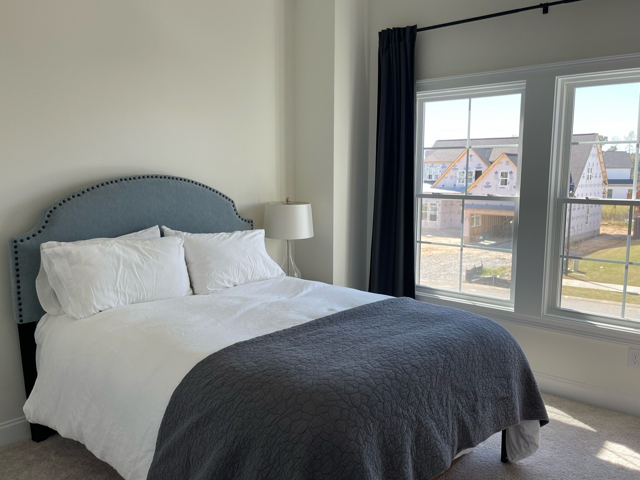 Ein Schlafzimmer mit Bett, Lampe, Fenster und Blick auf Häuser.