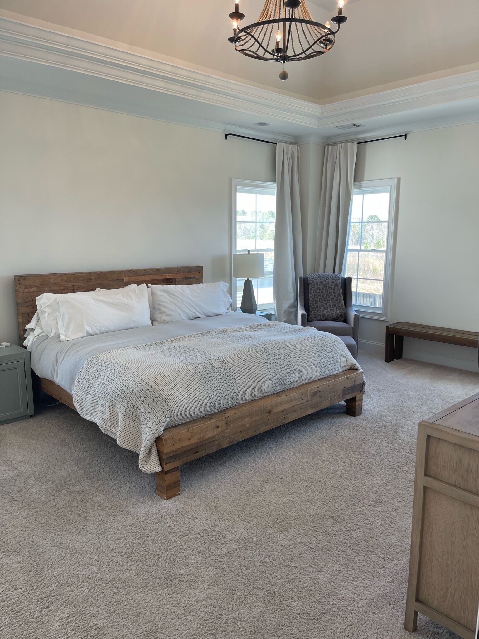 A bedroom with a wooden bed, a bench, a chair, a lamp, and a chandelier.