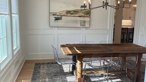 Ein Essbereich mit einem Holztisch, transparenten Stühlen, einem gemusterten Teppich und einem Gemälde einer Küstenlandschaft.