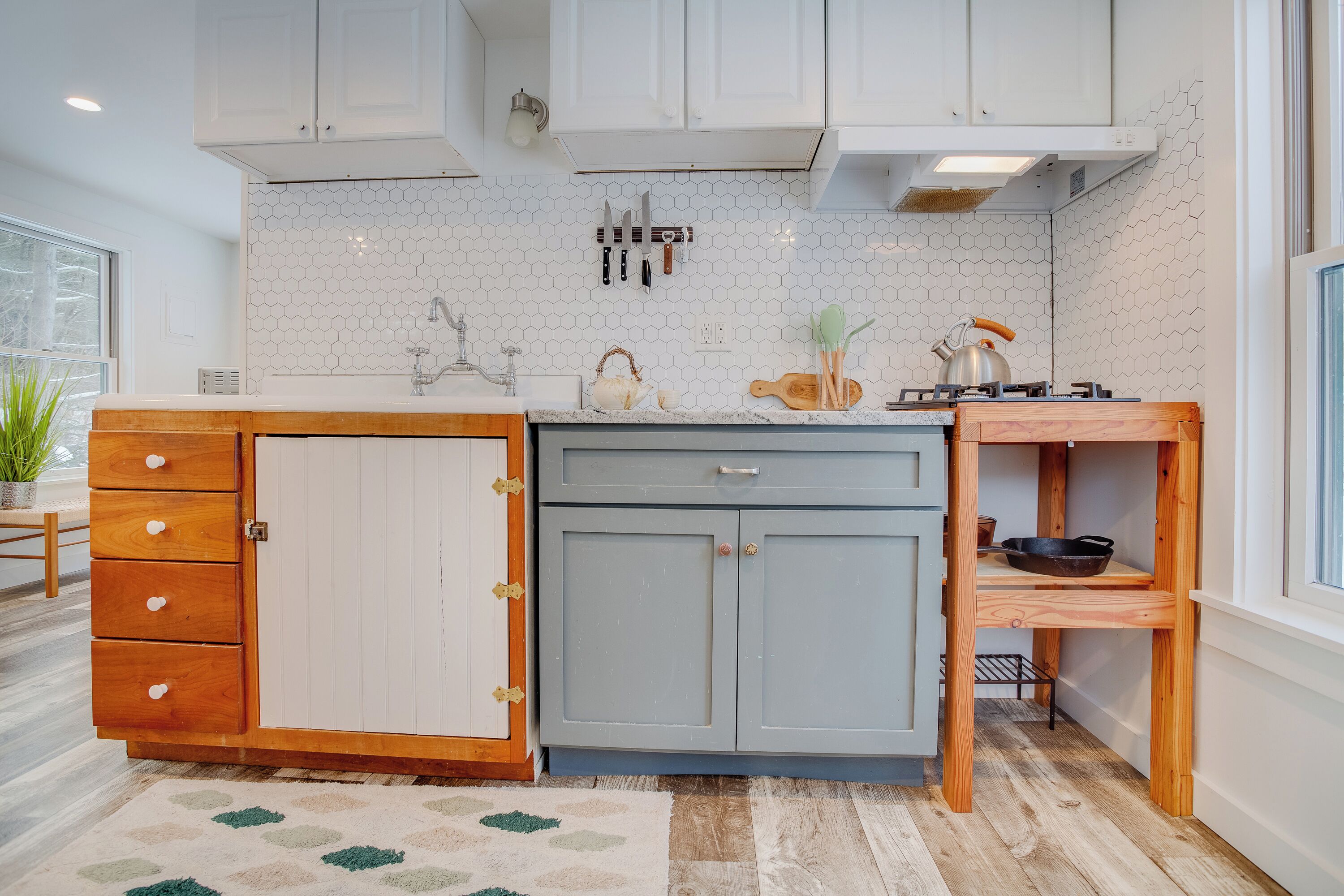 A kitchen with white cabinets, a hexagonal tile backsplash, and wooden drawers.