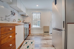A kitchen with white cabinets, a wooden countertop, a window, and a refrigerator.