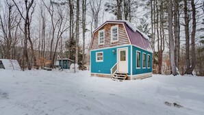 A small, single-story cabin with a red roof, surrounded by snow-covered ground and trees. - Tiny Acres: A Storybook Tiny Home, 4 Mi. to CDP (Milford)