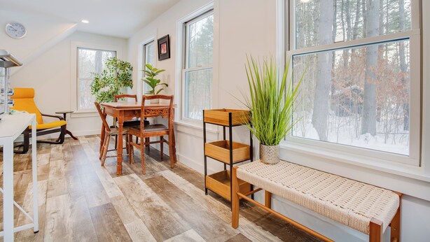 A room with a dining table, chairs, a bench, potted plants, and large windows with a view of trees. - Tiny Acres: A Storybook Tiny Home, 4 Mi. to CDP (Milford)