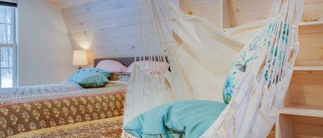 A room with a bed, a hammock chair, and a wooden ceiling.