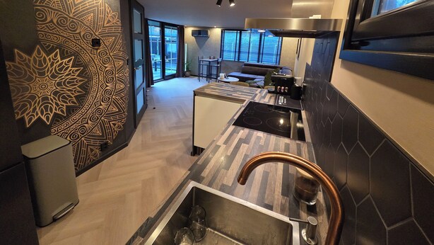 A modern kitchen with a patterned wall, a large window, and a stainless steel range hood. - Exclusive wellness bungalow, 6 person Jacuzzi! Woodland Wellness Resort (Ermelo)