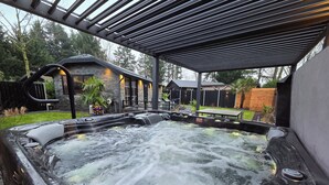 A hot tub with a waterfall feature, surrounded by a covered patio area with a pergola overhead. - Exclusive wellness bungalow, 6 person Jacuzzi! Woodland Wellness Resort (Ermelo)