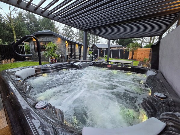 A hot tub with a waterfall feature, surrounded by a covered patio area with a pergola overhead.