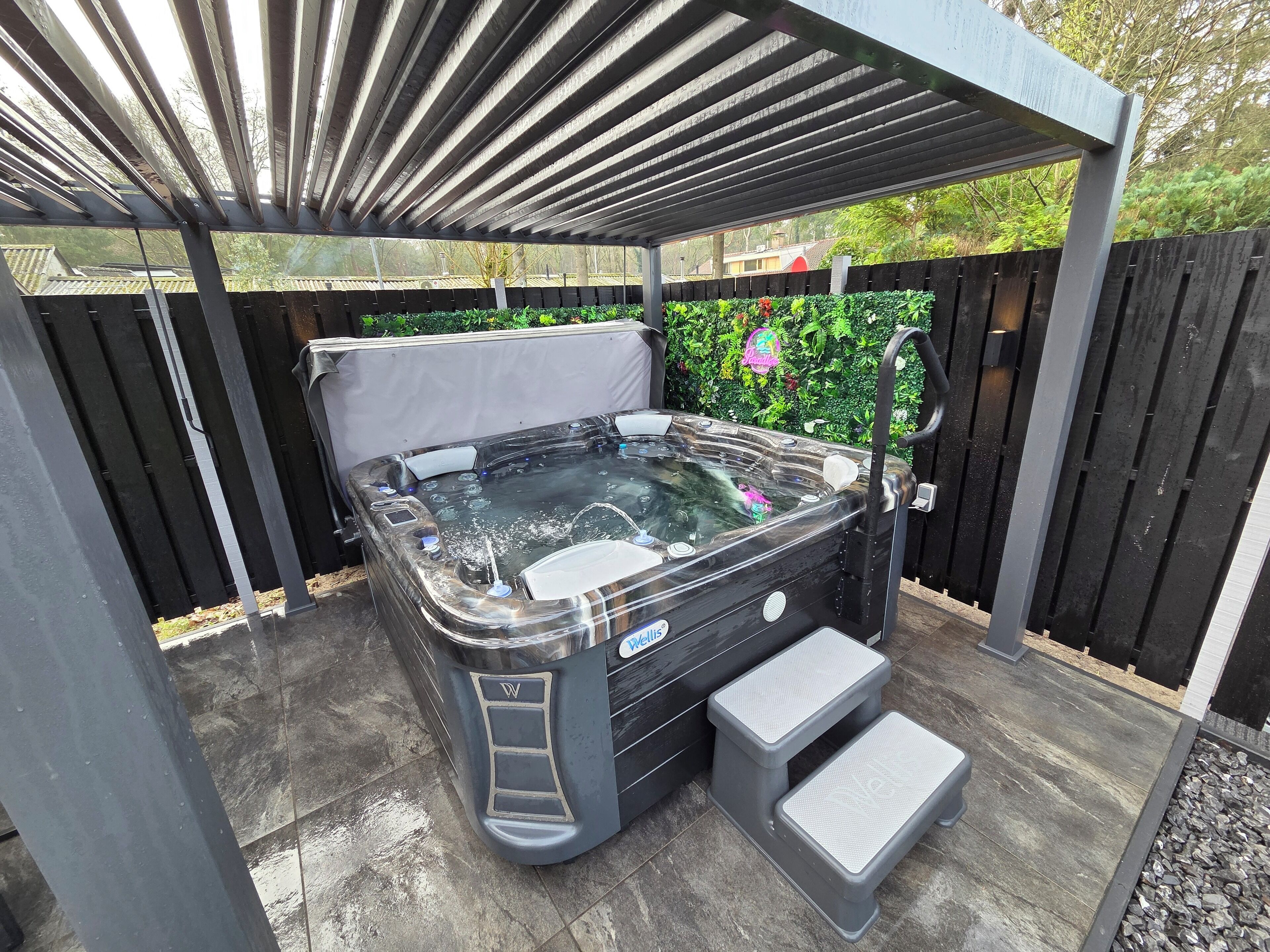 Un jacuzzi bajo una pérgola, con un cerco de madera y follaje al fondo.