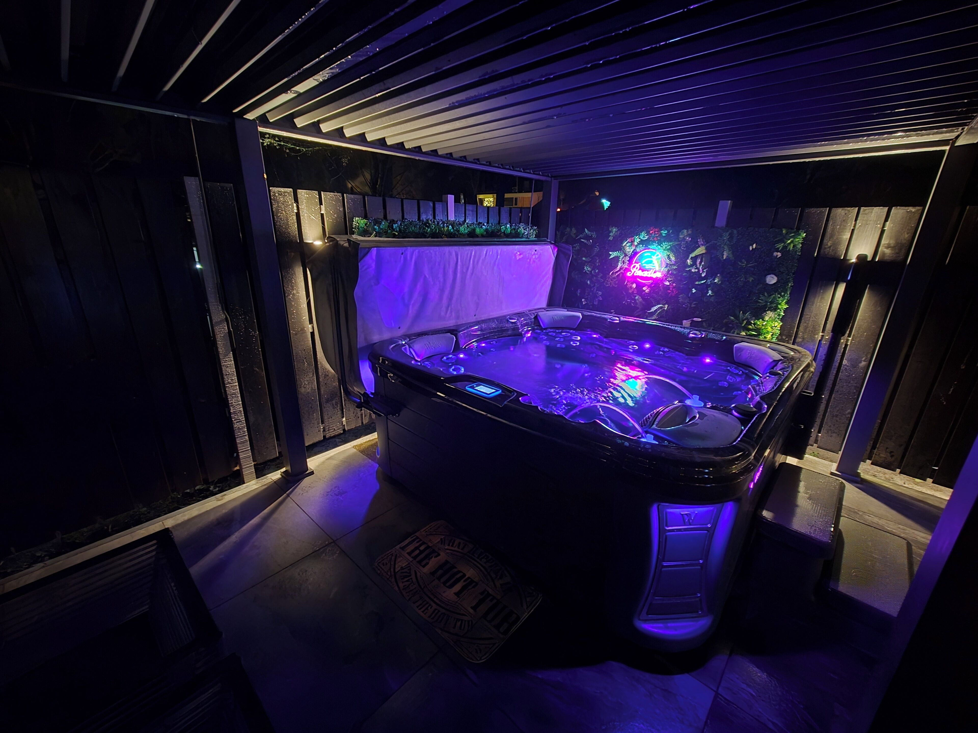 A hot tub with LED lighting, surrounded by a dark room with a wooden floor and a tiled wall.