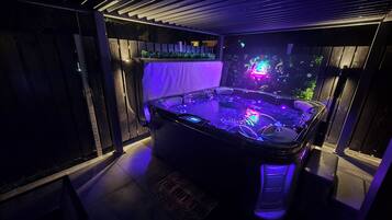 A hot tub with LED lighting, surrounded by a dark room with a wooden floor and a tiled wall.