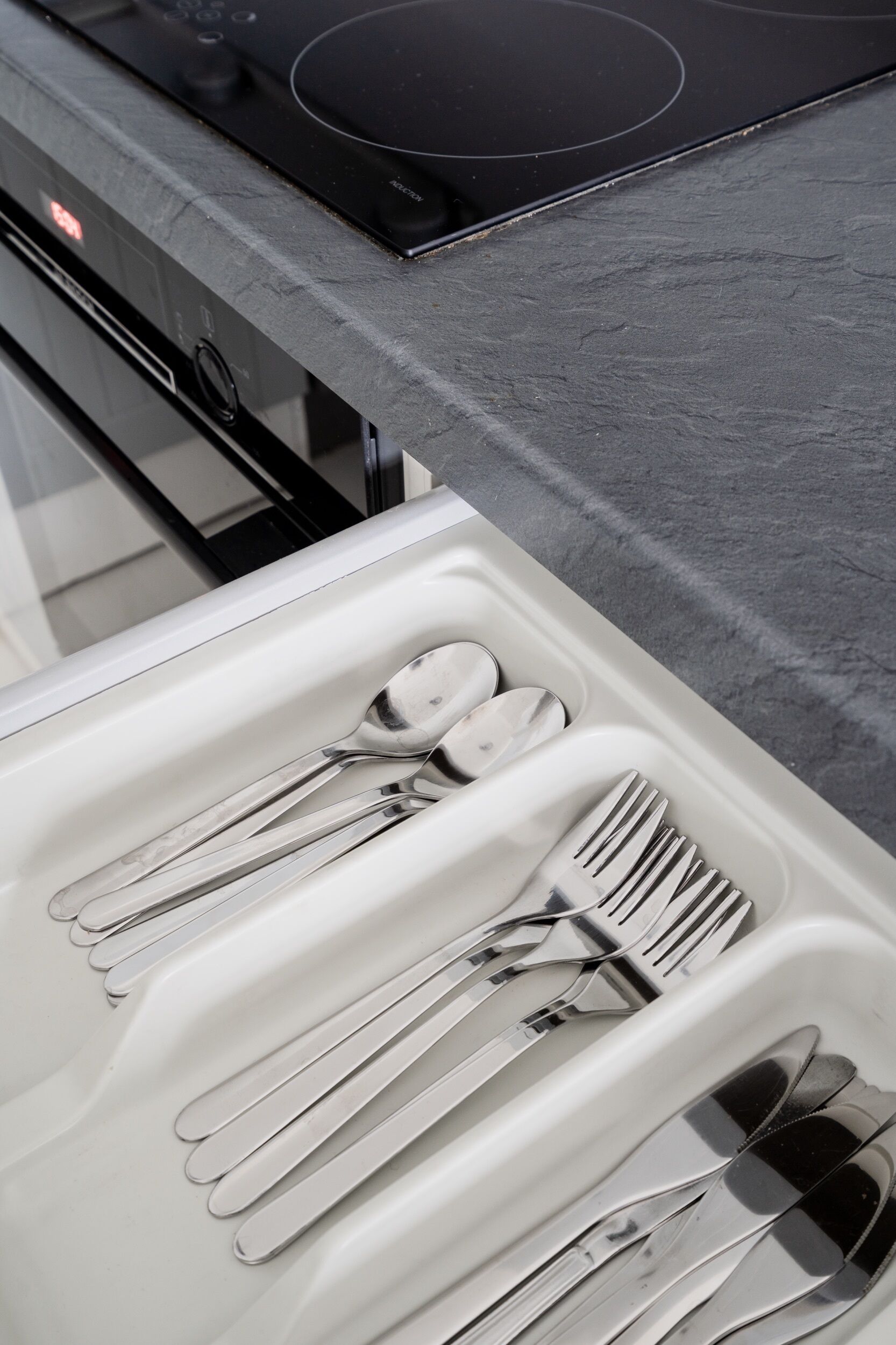 A drawer with utensils, a black induction cooktop, and a white countertop.