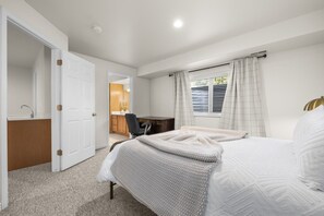 A bedroom with a bed, a desk, and a chair. There is a window with curtains and a view of the outside. - A newly renovated mountain basecamp with two king suites, perfect for families exploring American Fork Canyon. (American Fork)