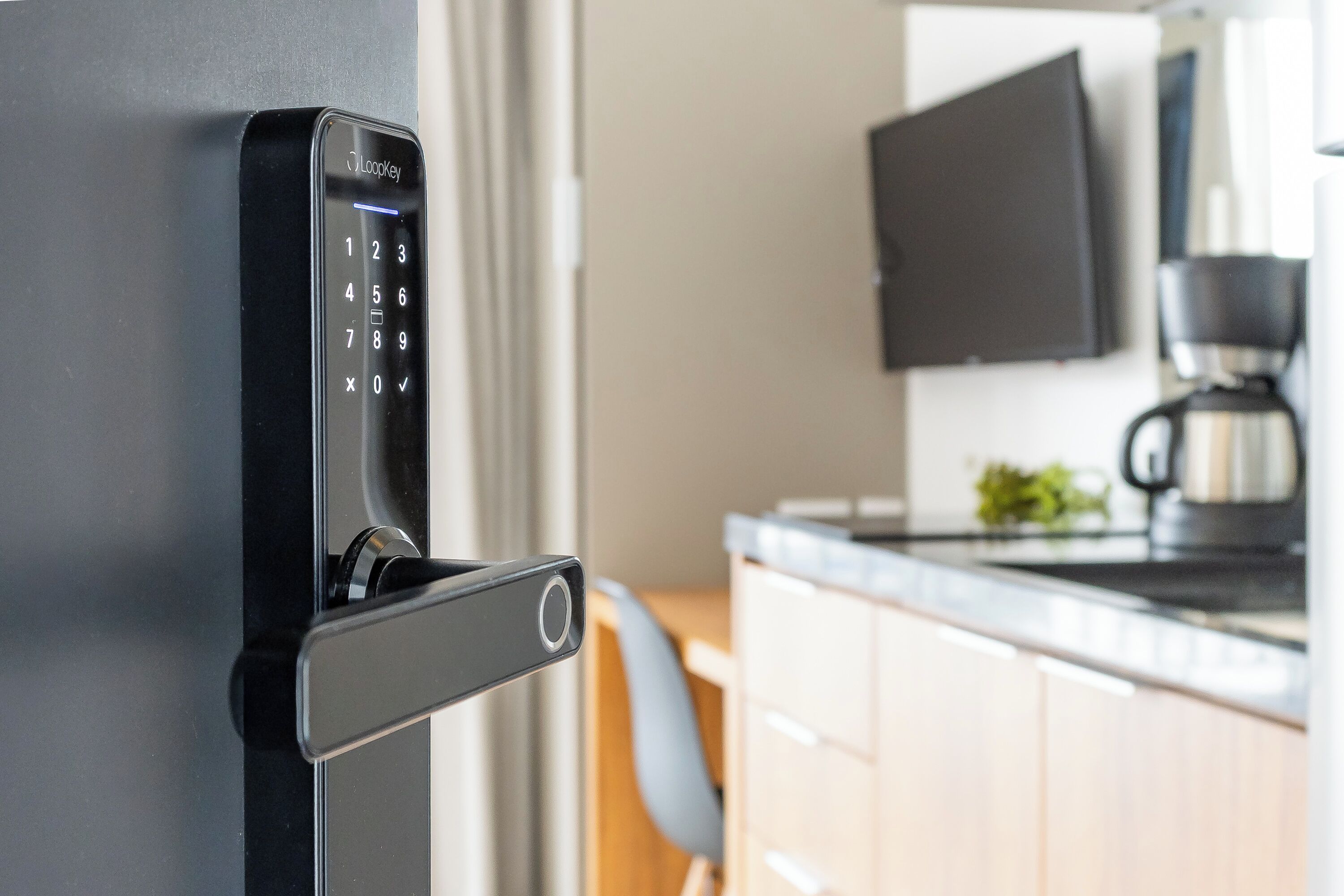 A modern kitchen with a built-in coffee machine, a flat-screen TV, and a door with a digital lock.