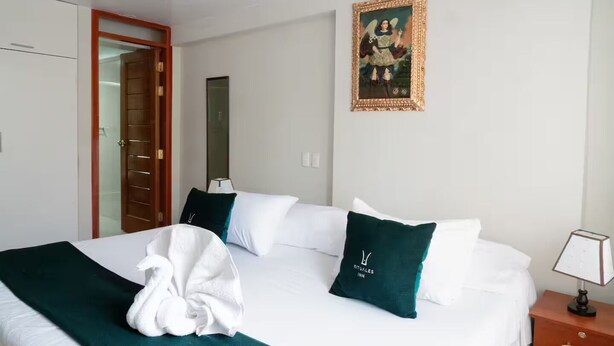 A hotel room with a bed, pillows, a robe, a nightstand, a lamp, a wardrobe, and a framed picture on the wall. - Apartment close to the main square + airport pickup (cusco)