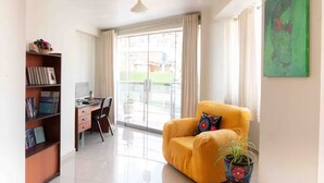 A modern living room with a desk, a yellow armchair, a bookshelf, and a large window. - Apartment close to the main square + airport pickup (cusco)