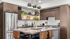 A modern kitchen with a central island, stainless steel appliances, wooden cabinets, and bar stools. - 3 Bed/3 Bath Cozy Mountain Retreat (Canmore)