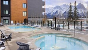 A pool area with lounge chairs and a view of mountains. - 3 Bed/3 Bath Cozy Mountain Retreat (Canmore)