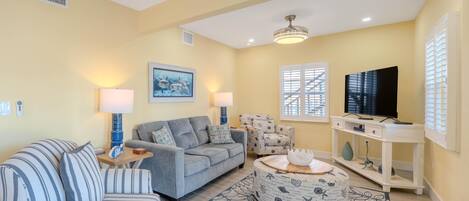 A living room with a sofa, armchair, ottoman, TV stand, and artwork on the wall.