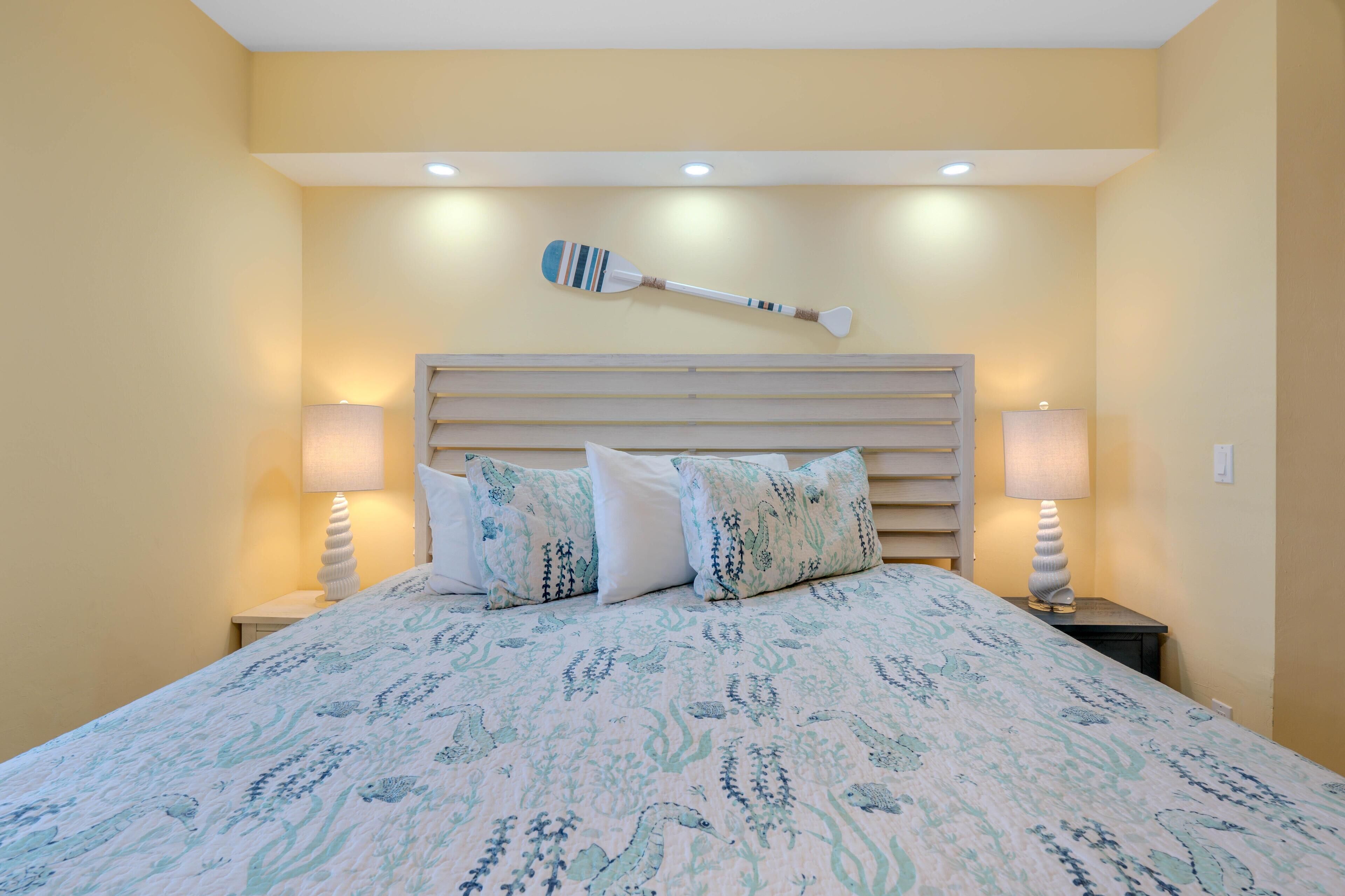 A bed with a patterned bedspread, two bedside lamps, a wall-mounted paddle, and a wooden headboard.
