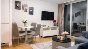 Un soggiorno moderno con zona pranzo, una TV a schermo piatto montata a parete e una porta scorrevole in vetro che dà su uno spazio esterno.
