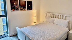 Una camera da letto con un letto bianco, un comodino, una lampada e tre quadri appesi al muro.