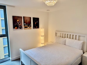 Ein Schlafzimmer mit einem weißen Bett, einem Nachttisch, einer Lampe und drei an der Wand befestigten Bildern.